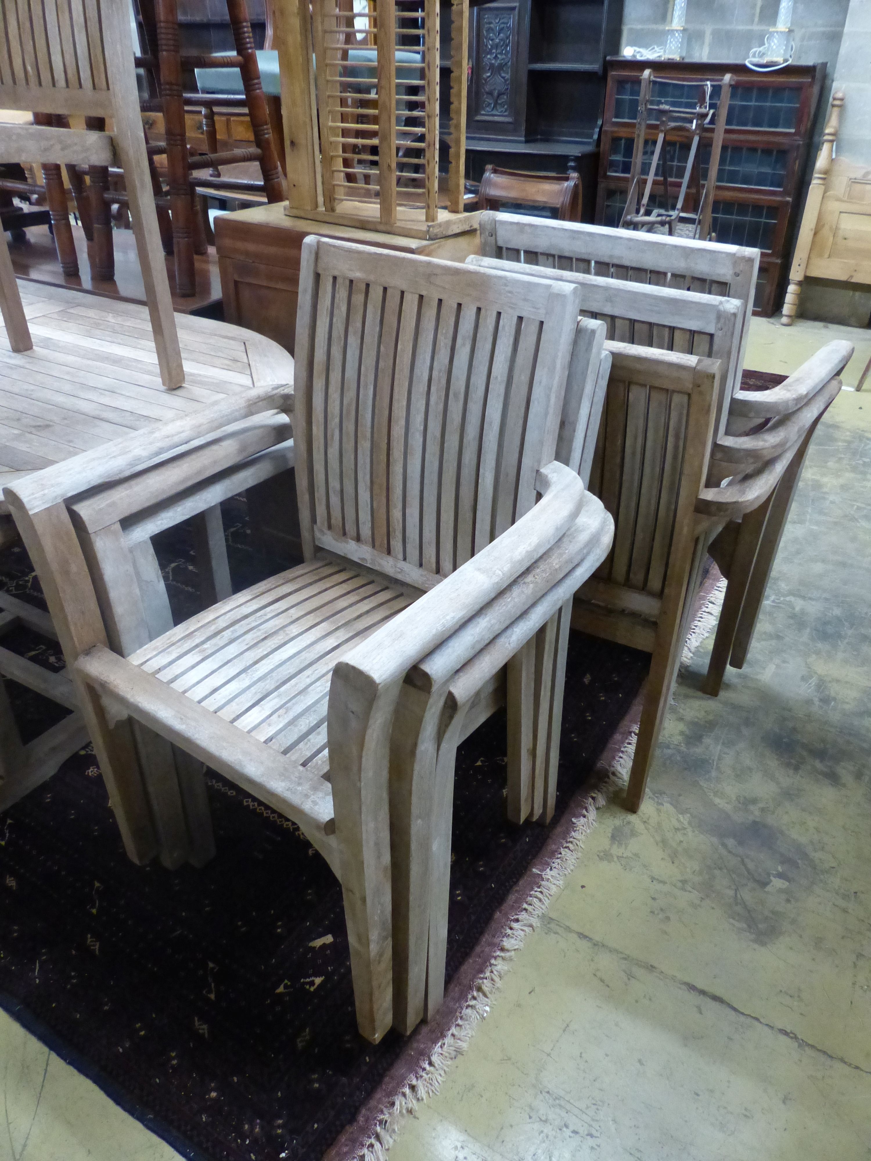 An oval weathered teak extending garden table, 240cm extended, width 100cm, height 74cm and eight stacking elbow chairs